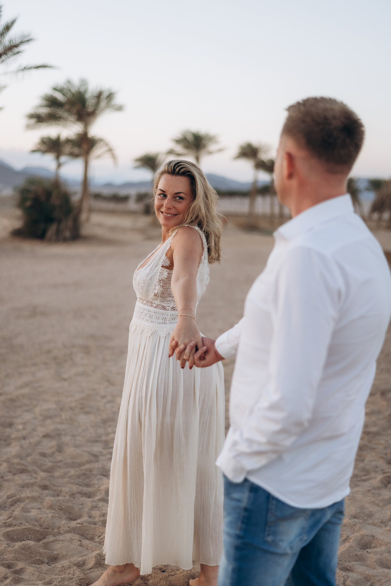 Hand in hand op het strand tussen palmbomen