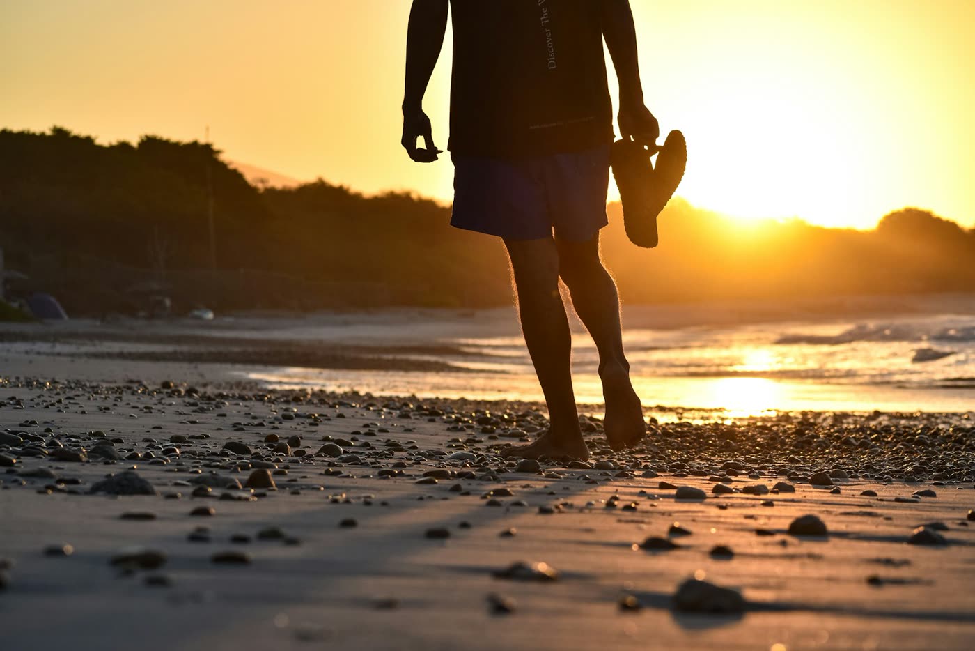 Op blote voeten met de schoenen in de hand over het strand bij zonsondergang